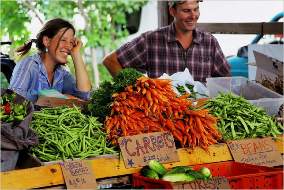 Two vegetable vendors at a market selling green beans, sweet carrots, beans and other vegetables.